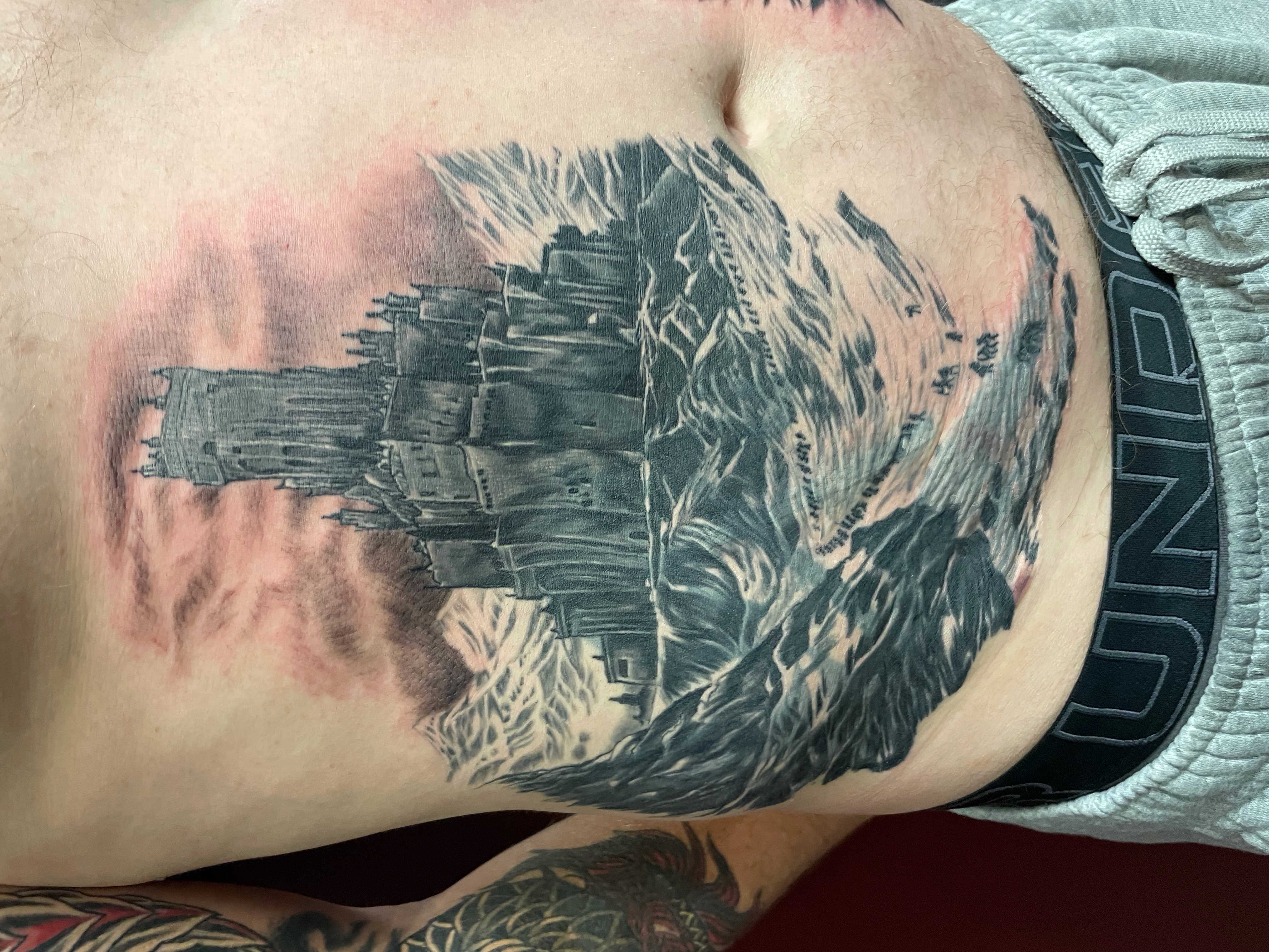 Black and grey gothic castle on stormy seas stomach piece cover-up by Jin