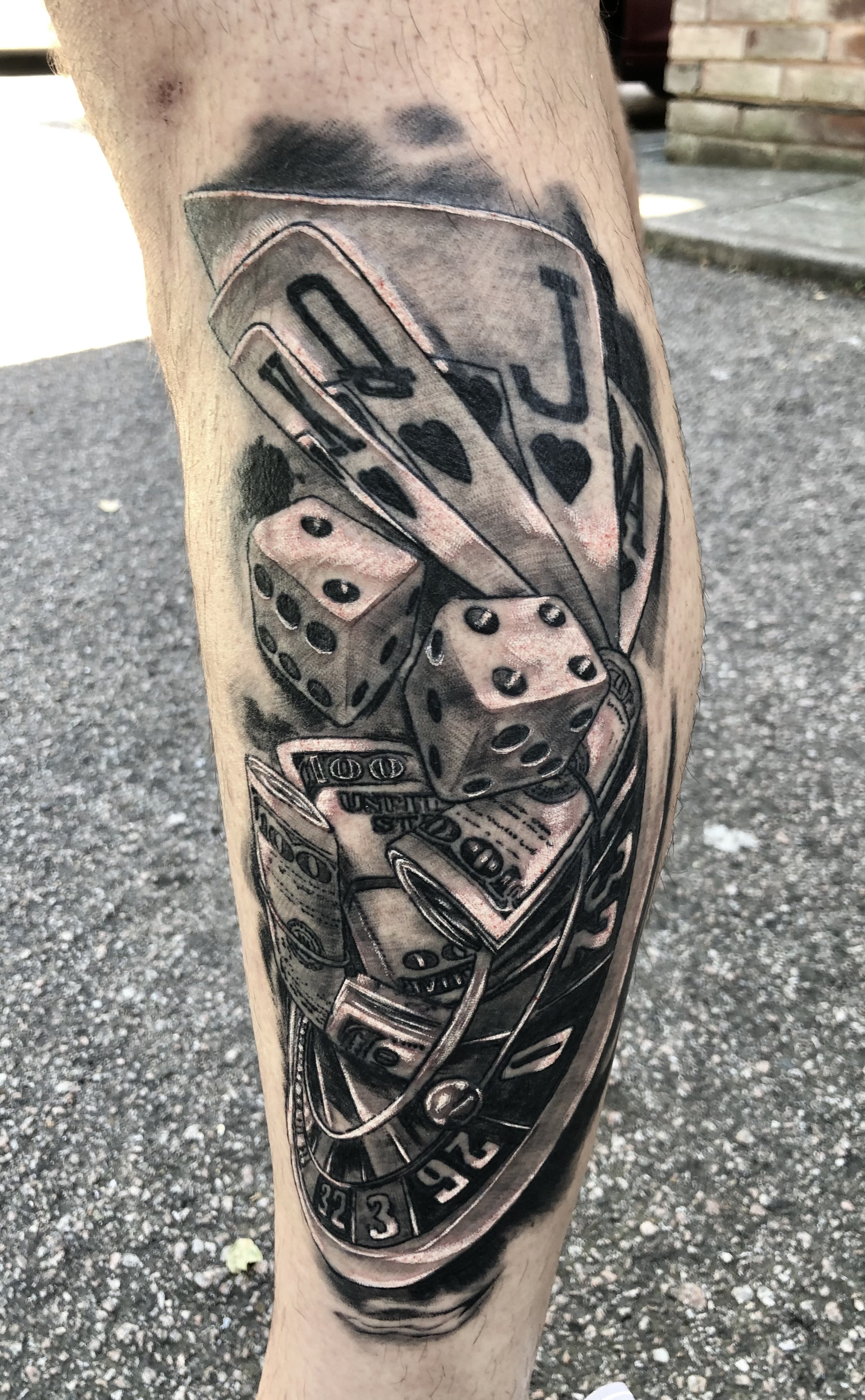 Black and grey gambling themed calf piece with playing cards, dice, roulette wheel and dollar bills by Jin